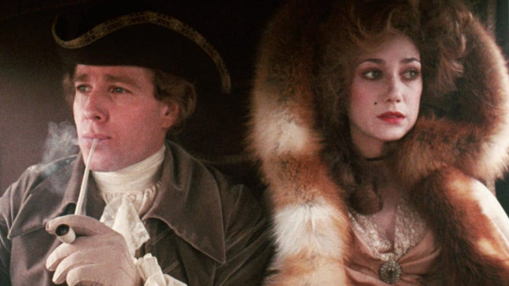 Man and woman sit side by side looking out a window, dressed in furs and formal wear