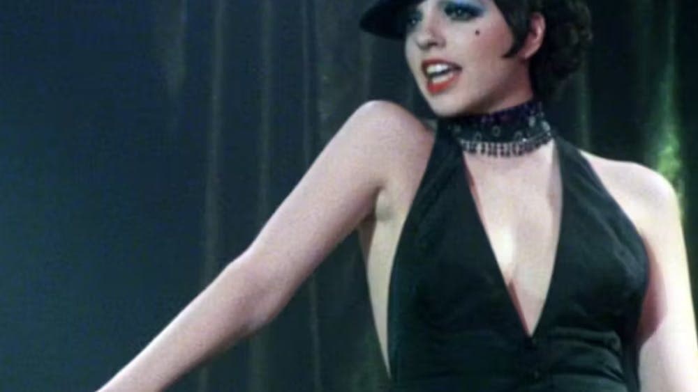 Woman with short black hair, hat and black top in the middle of singing looking over right shoulder