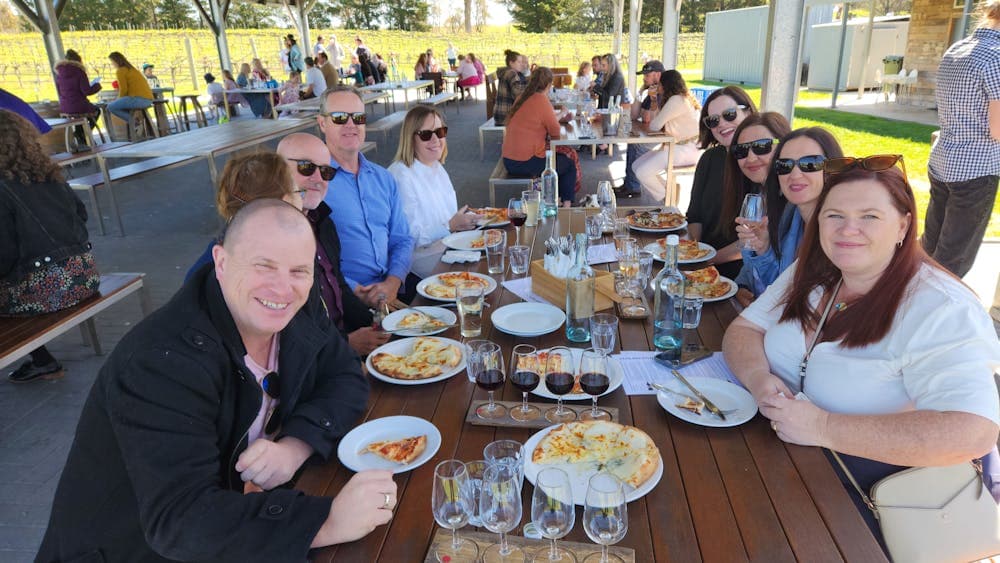 A group of people sitting at a table enjoying a meal together, with a variety of food and glasses of