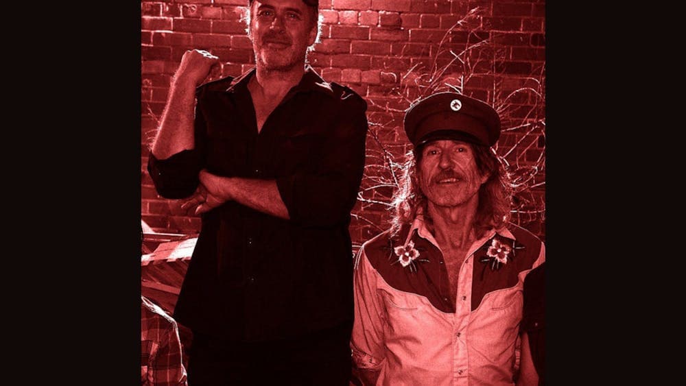 A photo of two men standing next to each other in front of a brick wall