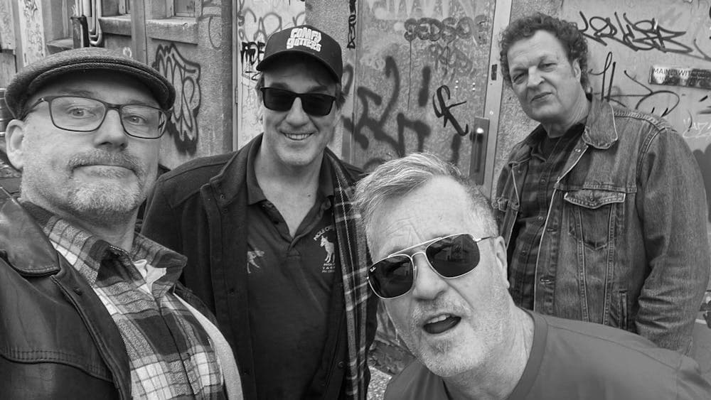 Four men standing in front of a wall with graffiti