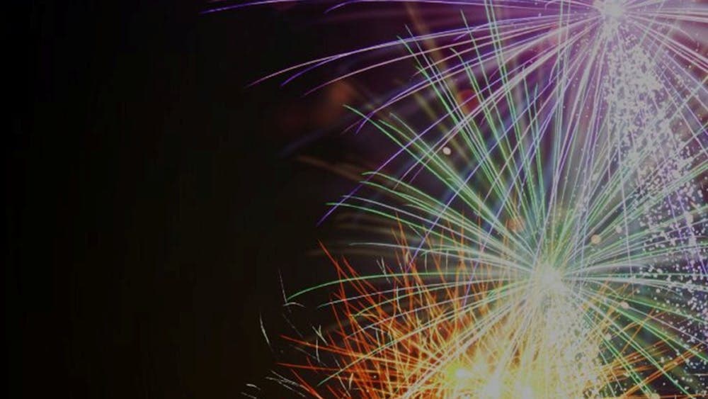 Magenta, green, yellow, orange fireworks exploding on right-hand side against a black background.