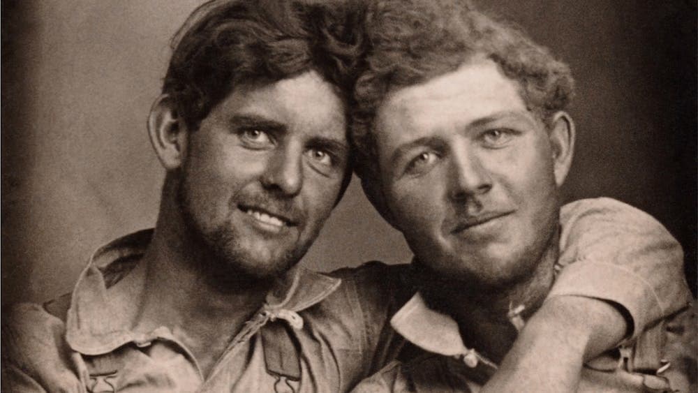 An archival photograph of two working men with an arm around the neck of the other