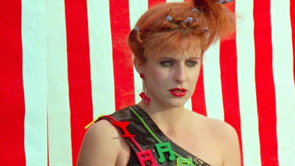 woman with red lipstick and 80's hairstyle looks glum past the camera, red and white stripe backgrou