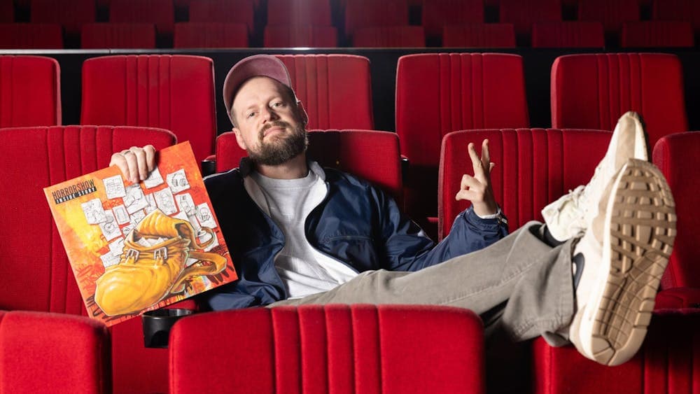 Man sitting in an empty cinema, feet up on seats with a cap, holding a vinyl cover