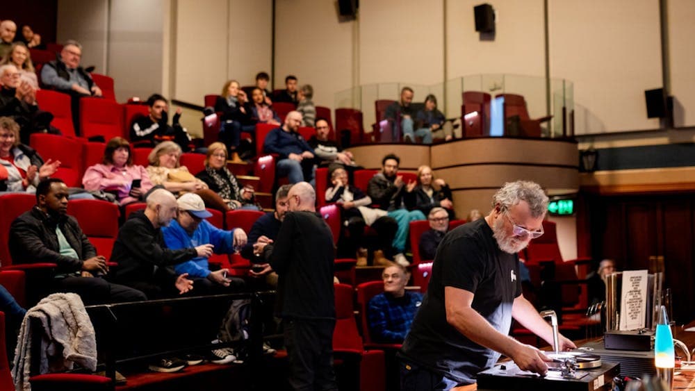 Audience in a theatre and a man at the front preparing to play a vinyl