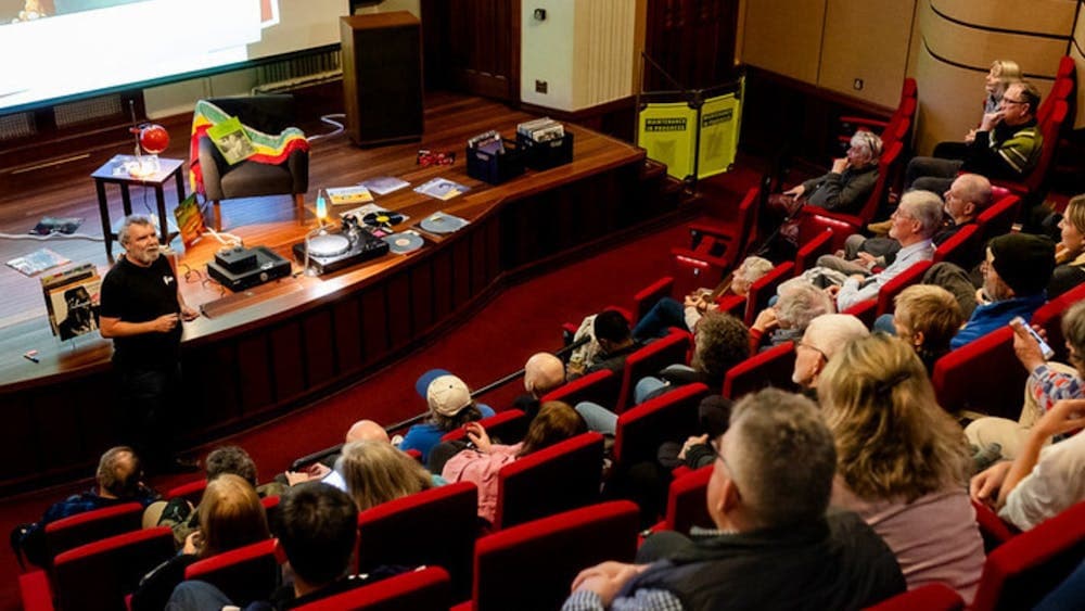 Audience in a theatre and a man at the front preparing to play a vinyl