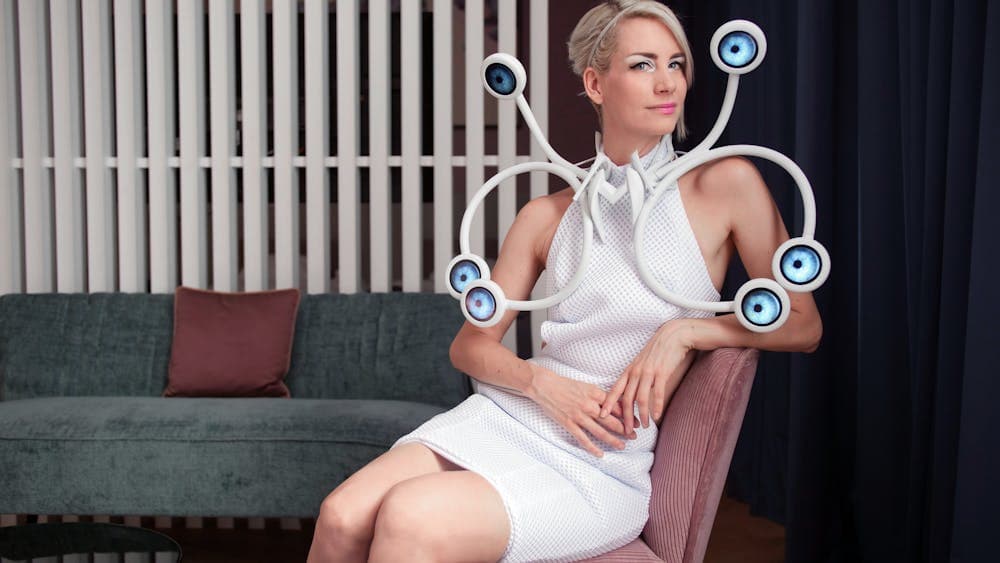 Anouk Wipprecht sitting in a seat wearing a white dress with curved tech elements