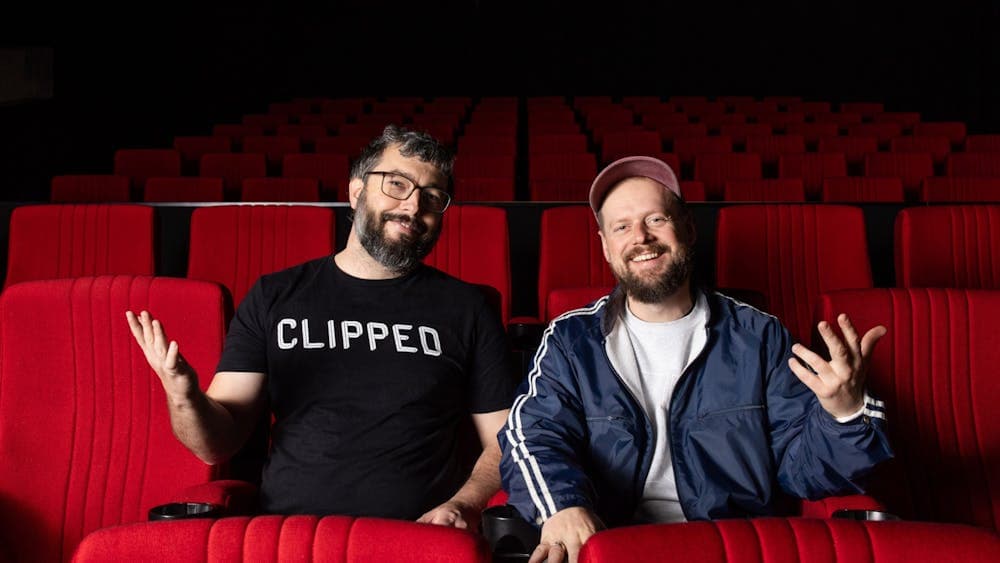 Two men sitting in an empty theatre smiling