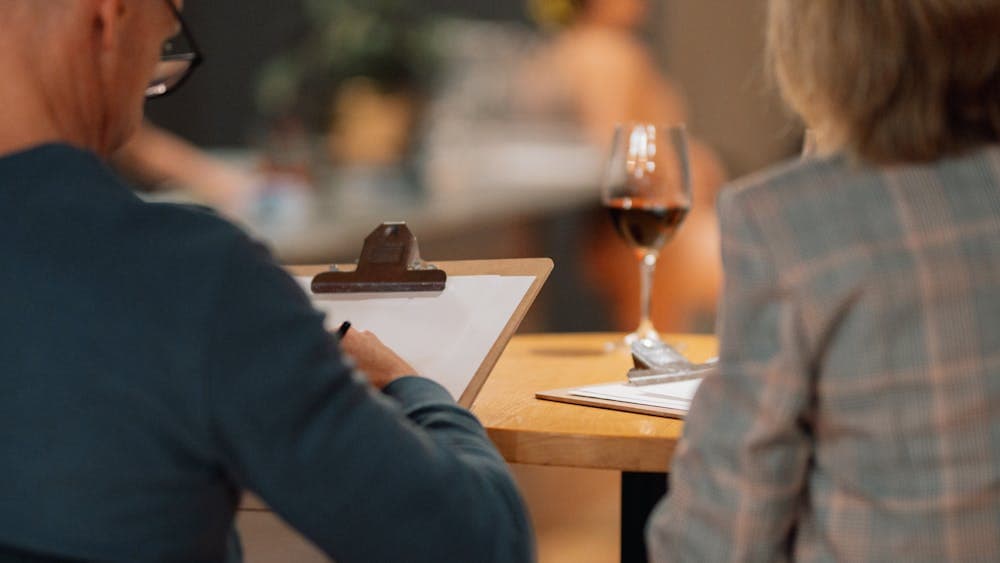 Two people drawing, with a glass of red wine on the table