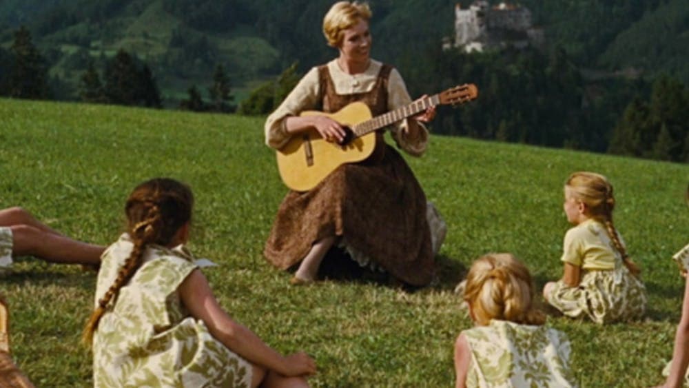 Woman in green field playing guitar to children sitting around her