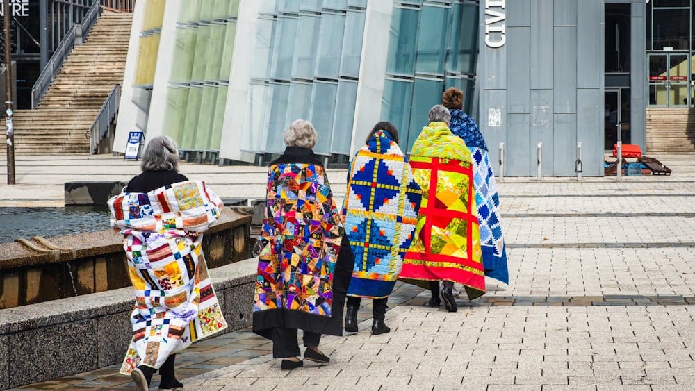 Canberra Quilters walking with colourful quilts over their shoulders through Civic Square
