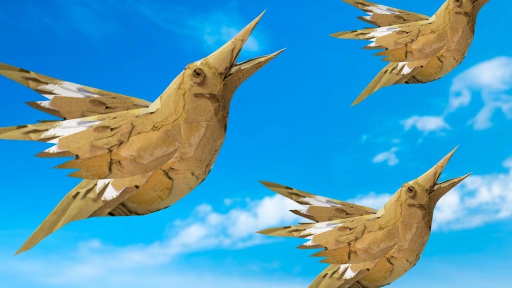 Three cardboard birds soar across a bright blue sky with soft clouds in the background.