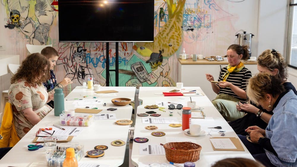 Workshop participants engaged in hands-on craft activities around a table in an art-filled studio.