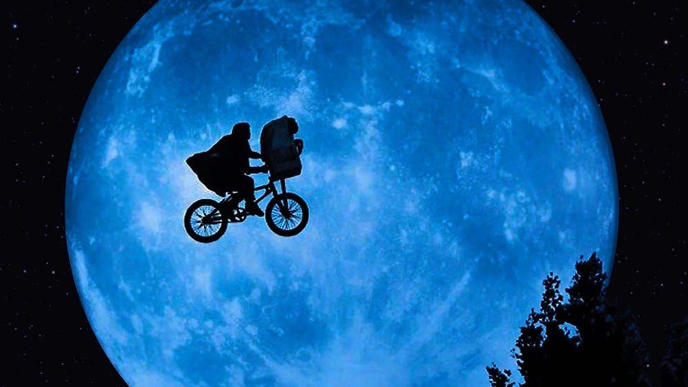 A shadow image of a person in a cape on a bike cycling across the sky in front of a large planet