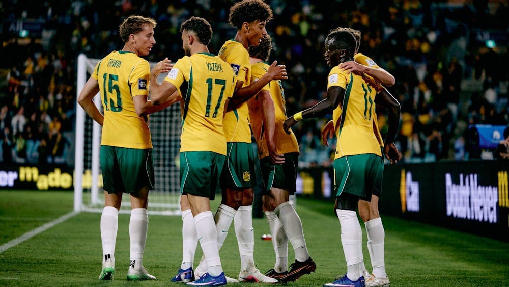 Soccer players in yellow kits celebrate a goal on a stadium pitch
