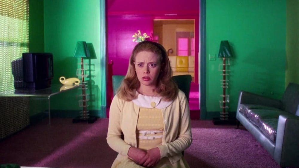 Woman sits in preppy outfit with her mouth open, pink door in background