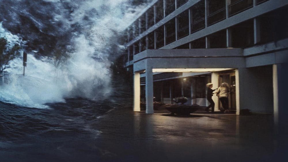 Still of two people running into a building while a wave larger than the image is coming towards the