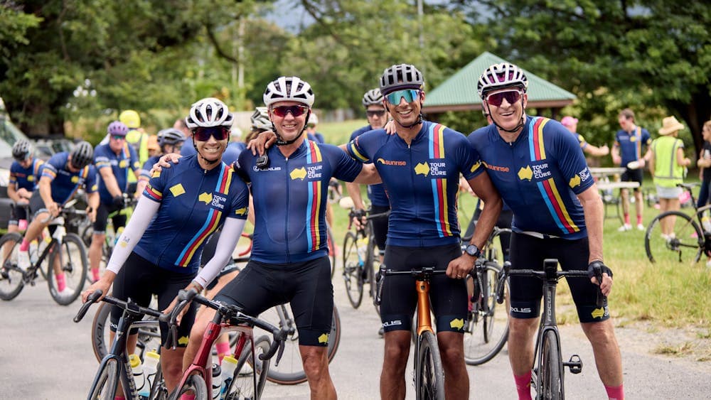 Four cyclists casually on bikes not riding inc. Ch7's Mark Beretta at the end of Signature Tour '25