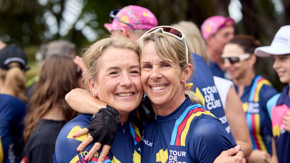 Two female cyclists embrace off-bike at the end of Signature Tour '25.