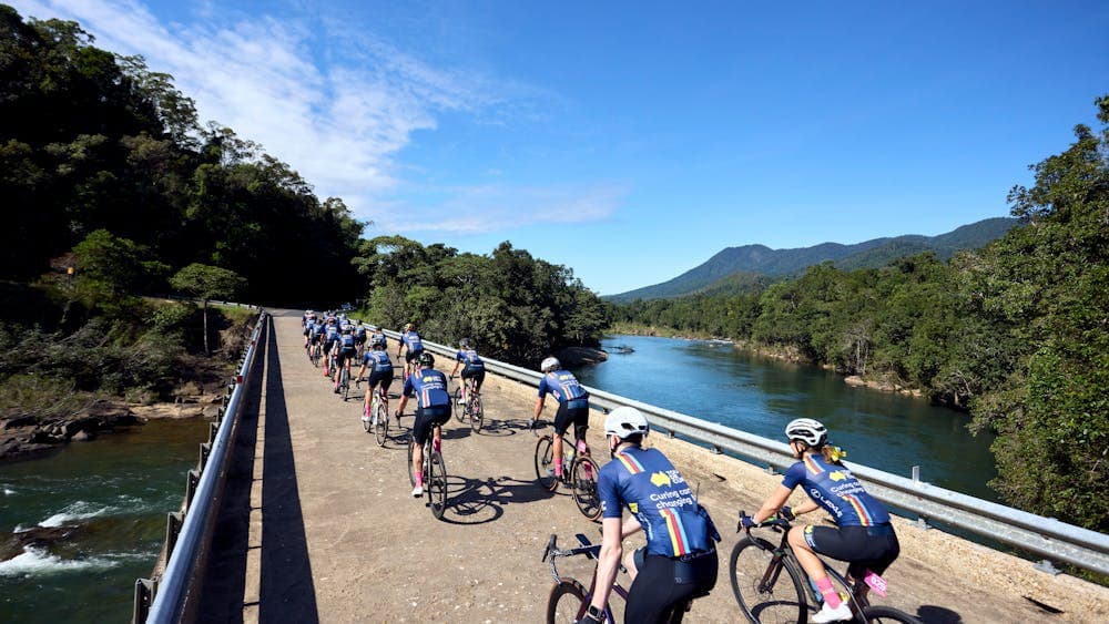 Cycle peloton crossing bridge in formation taken from behind cyclists, scenic