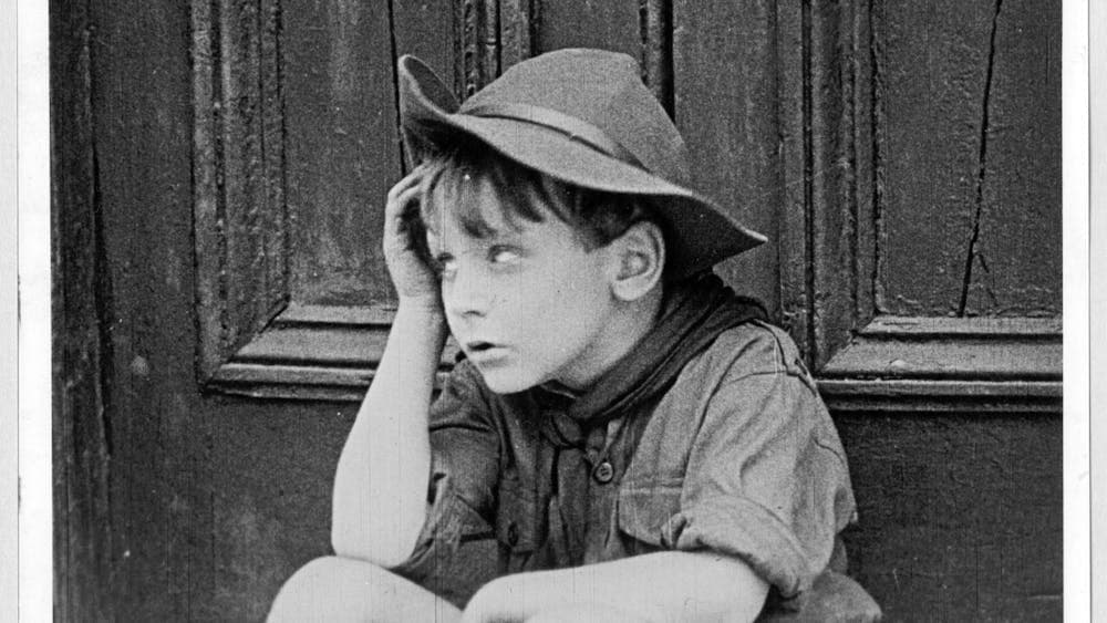 Black and white film still of young boy wearing hat rolling his eyes