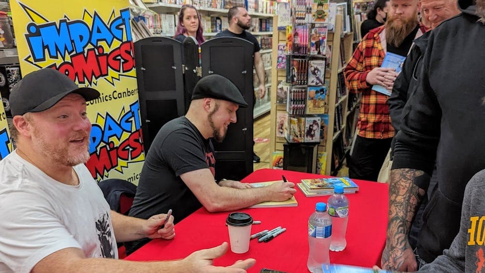 Two men sit at a table a line of people waiting to meet them