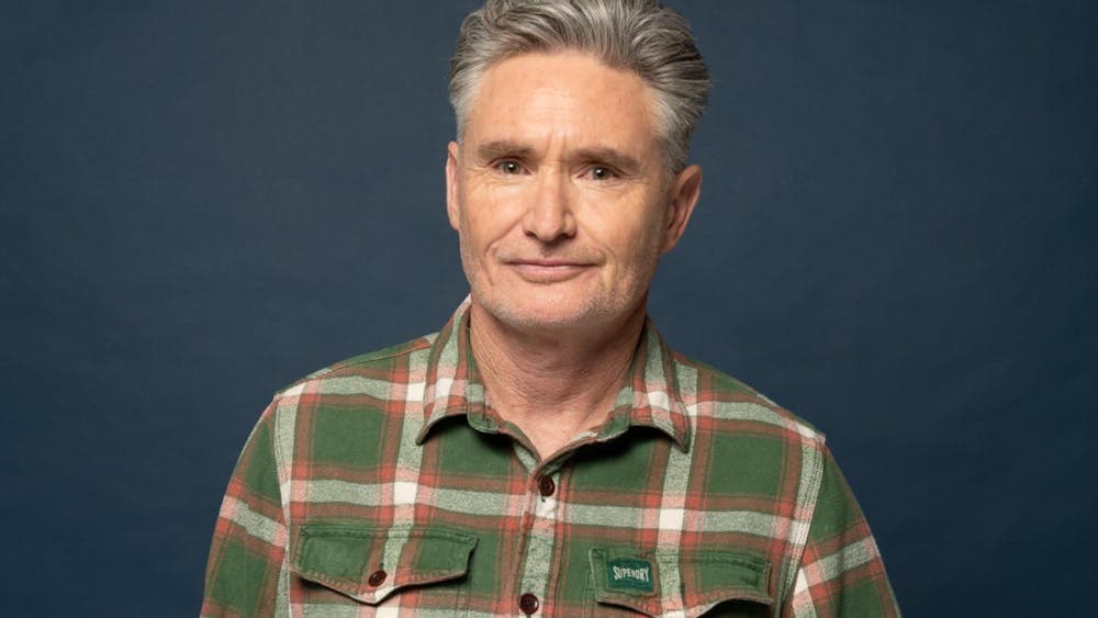 Comedian Dave Hughes standing in front of a dark background