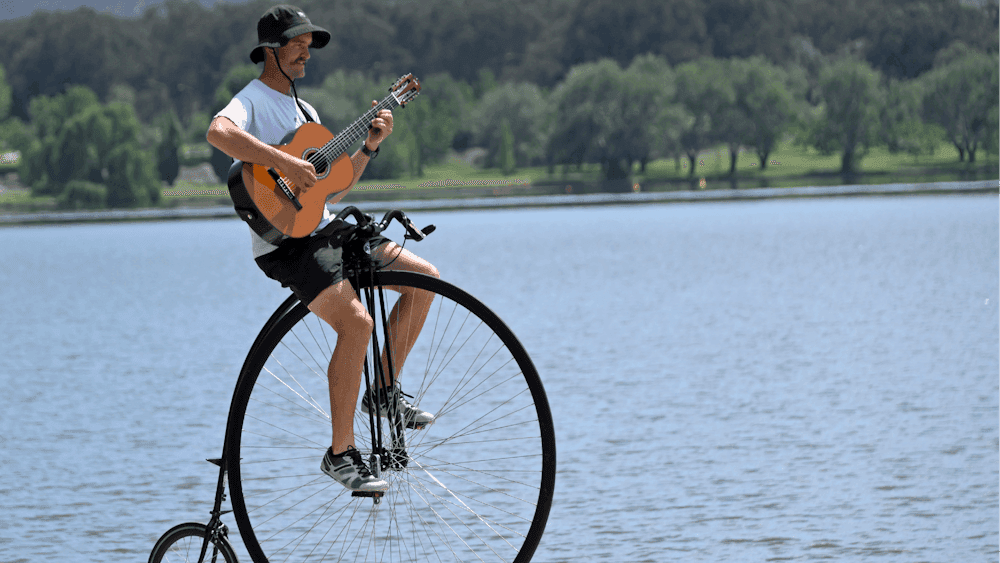 Simon playing a guitar while riding his penny-farthing