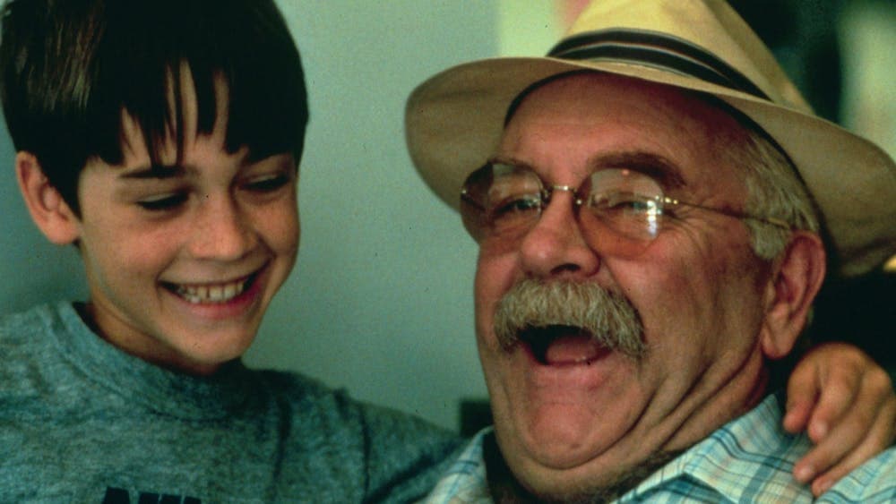 Older man wearing a hat and glasses looking happy with a young boy next to him with his arm around h