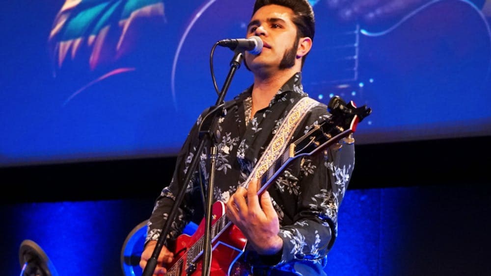 A First Nations Australian man playing a red guitar and singing into a microphone.