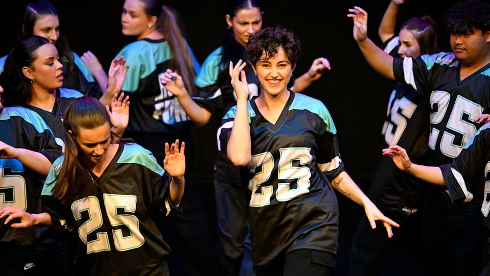 A group of young dancers with the central dancer looking up and smiling. All wearing #25 jersey.