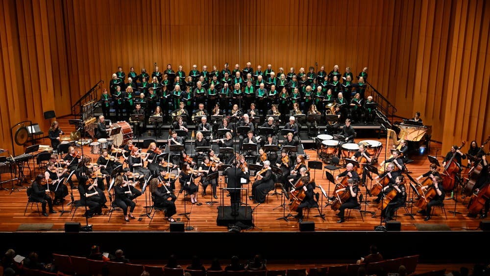 Large orchestra, piano and choir on stage with Louis Sharpe conducting.