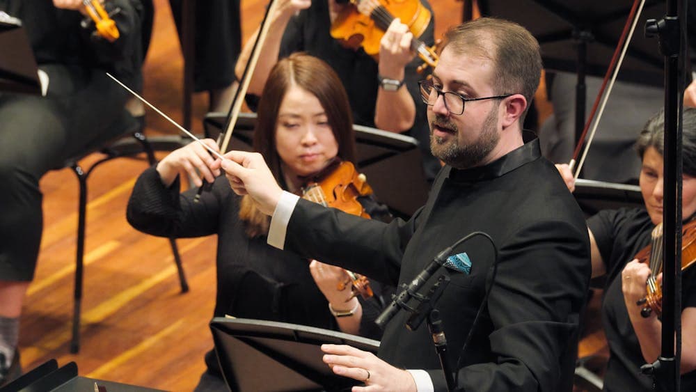 Louis Sharpe conducting performance with female violin players in the background