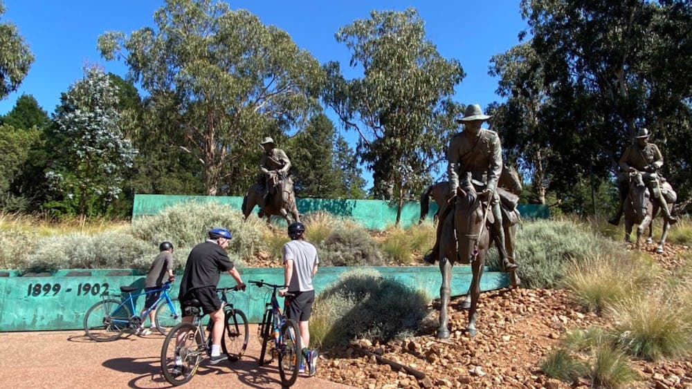 People on bikes at the Boer War memorial, which features sculptures of large humans on large horses.
