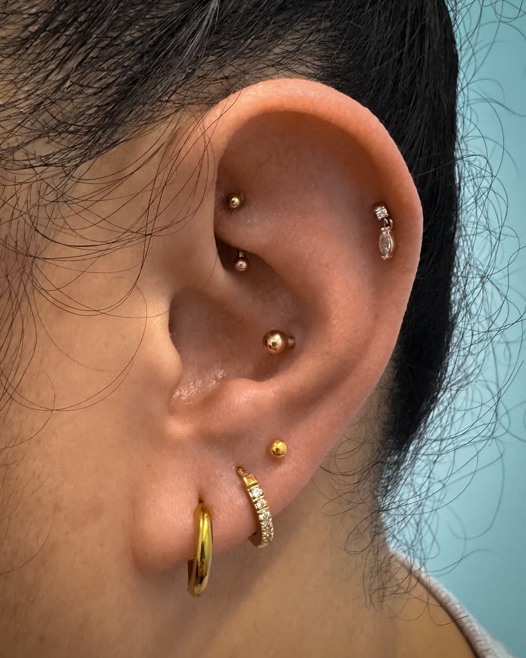 Close up photo of an ear with eight stud and ring earrings