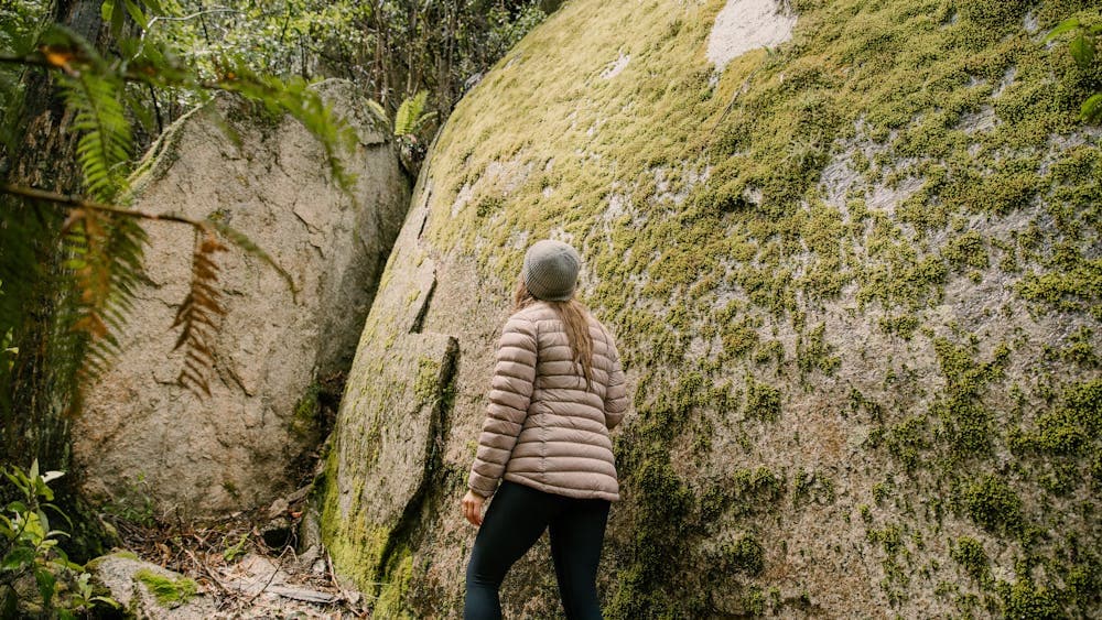 Woman hiking beside huge moss covered granite boulder