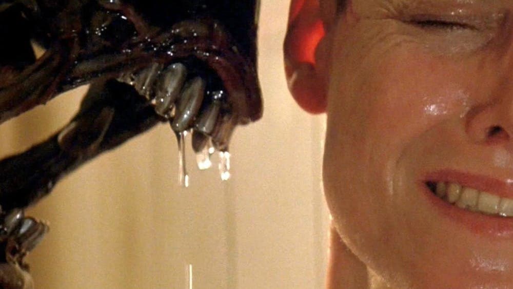 Woman looking scared on right with alien figure with dripping teeth threatening her