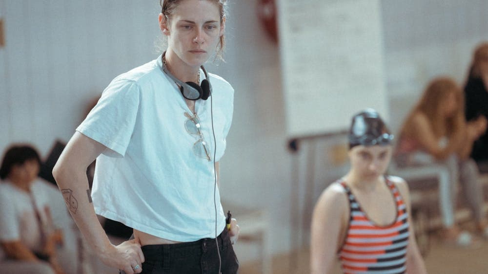 Woman stands with headphones and white t shirt with hands in pockets looking forlorn