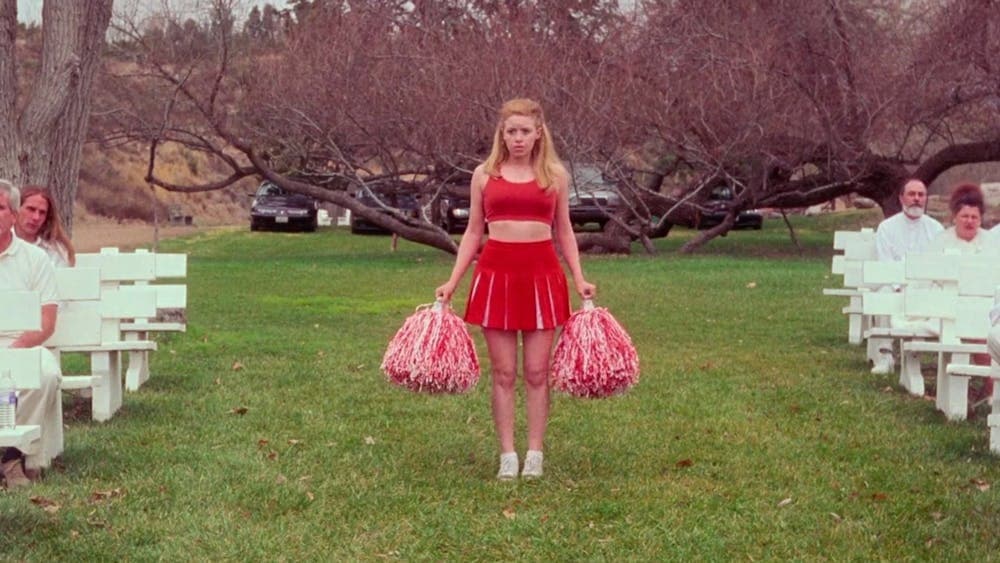 Cheerleader stands between white seating arrangement on green grass