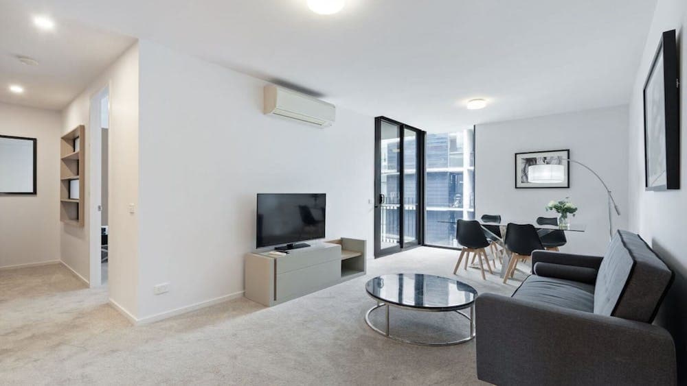 Modern apartment living room with grey sofa, TV, coffee table, and balcony doors.