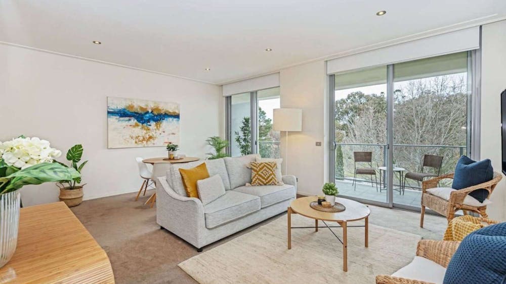 Bright living room with light grey sofa, wooden coffee table, and glass balcony doors.