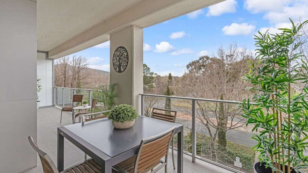 Covered balcony with outdoor dining table and leafy green views.
