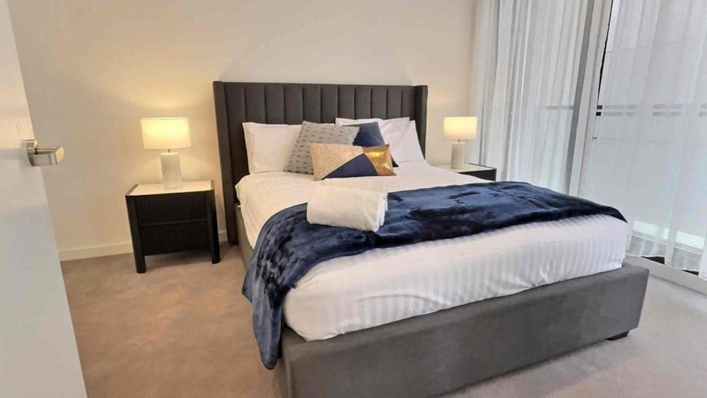 Modern bedroom with a grey tufted bed, navy throw blanket, bedside tables, and lamps.