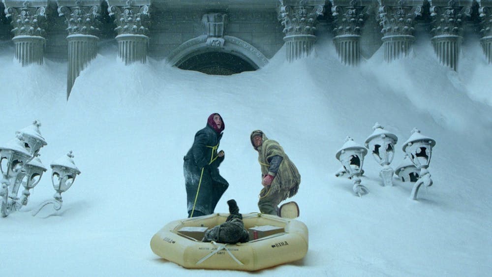 Two men in snow pulling a blow up boat looking scared and cold
