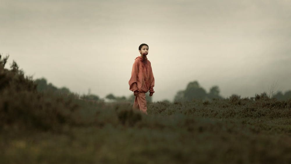 Young child with shaved head stands in isolated surrounds with blood around mouth