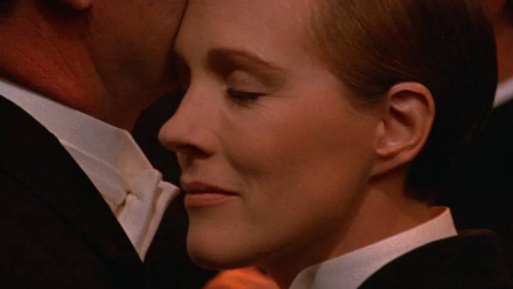 Close up of woman dressed in tuxedo with eyes closed pressed against chin of another person