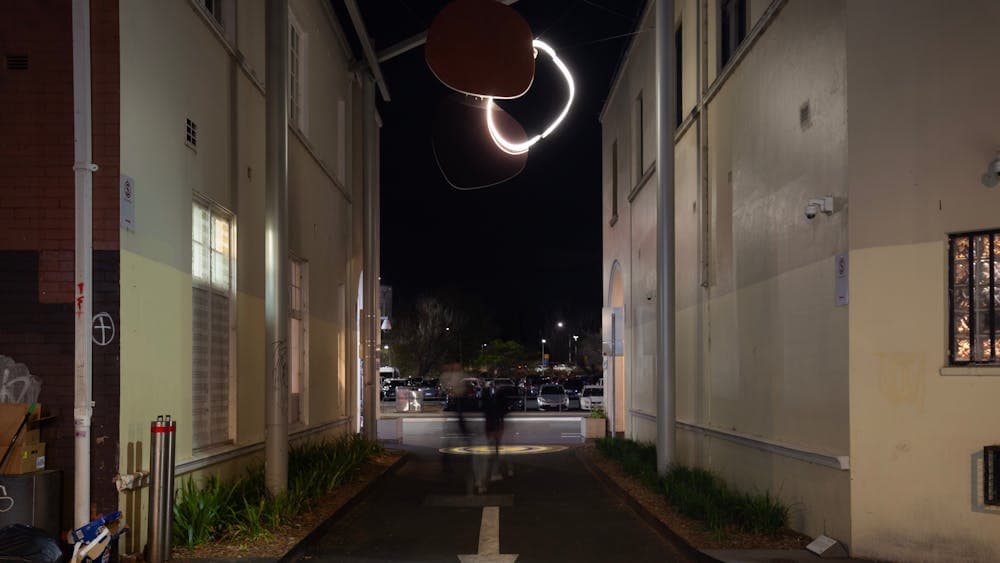 A neon sculpture hanging in an alley way at night.