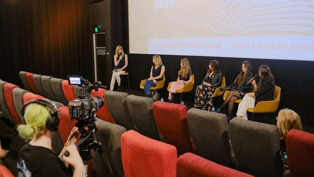 The image depicts a panel discussion taking place in front of a cinema screen