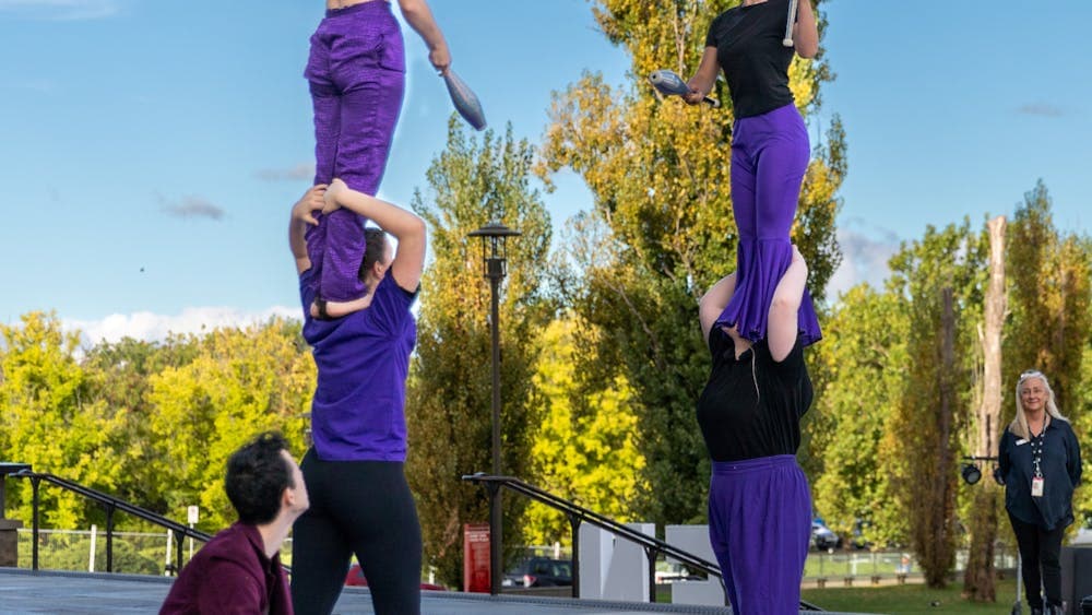 Warehouse Circus artists juggle to each other while balanced on shoulders